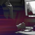 Person using a computer with hand on mouse and chin resting on another hand. Screen shows an indistinct image. Dark environment with light streaks across the foreground.