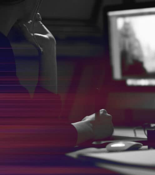 Person using a computer with hand on mouse and chin resting on another hand. Screen shows an indistinct image. Dark environment with light streaks across the foreground.