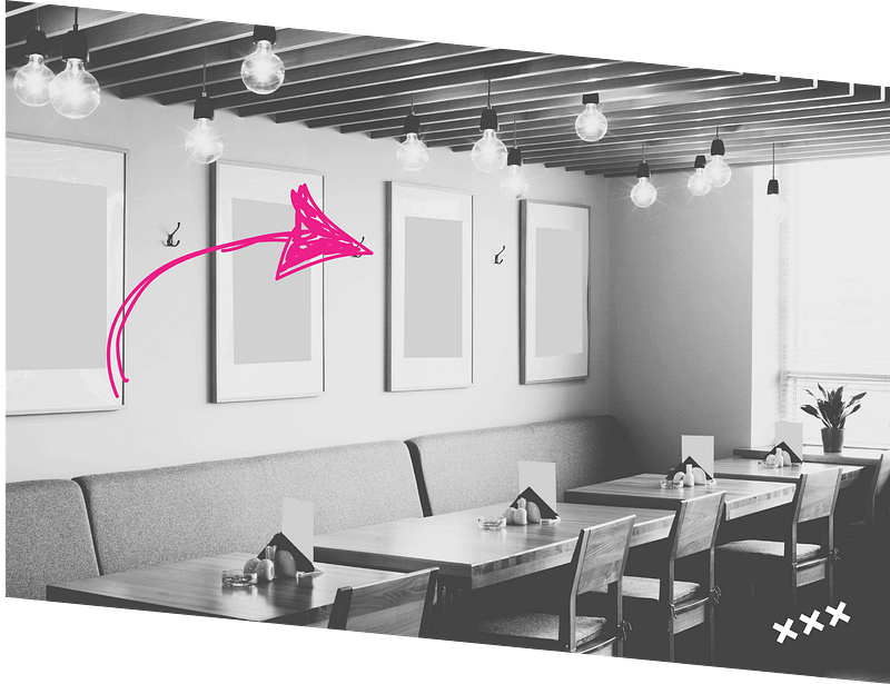 A black and white cafe interior with modern lighting, framed art on the wall, and neatly arranged tables and chairs. A pink arrow points to one of the framed pictures.